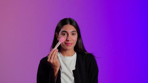 العناية بالجمال والمظهر الخارجي، مكياج وميكاب تتوريال, مفهوم التزين والتجمل، بورتريه مقرب لامرأة عربية خليجية  سعودية ترتدي الزي الكاجوال تستعمل فرشاة أحمر الخدود, خلفية ملونه