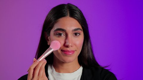 مكياج وميكاب تتوريال، العناية بالجمال من خلال أدوات ومستحضرات التجميل, مفهوم التزين والتجمل، بورتريه مقرب لامرأة عربية خليجية  سعودية ترتدي الزي الكاجوال تستعمل فرشاة أحمر الخدود, خلفية ملونه