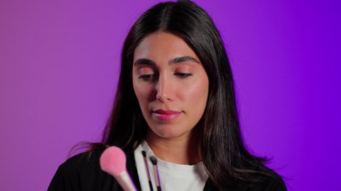 تطبيق مستحضرات المكياج للحفاظ على المظهر, مفهوم التزين والتجمل، بورتريه مقرب لامرأة عربية خليجية  سعودية ترتدي الزي الكاجوال تستعمل فرشاة أحمر الخدود, خلفية ملونه