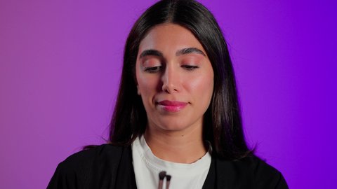 العناية بالمظهر عبر المستحضرات التجميلية، مفهوم التزين والتجمل, بورتريه مقرب لامرأة عربية خليجية سعودية ترتدي الزي الكاجوال تستعمل فرشاة ظل العيون, خلفية ملونه