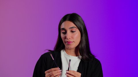 تطبيق مستحضرات التجميل للعناية بالبشرة، العناية بالجمال والمظهر الخارجي، مفهوم التزين والتجمل, بورتريه مقرب لامرأة عربية خليجية سعودية ترتدي الزي الكاجوال تستعمل فرشاة ظل العيون, خلفية ملونه