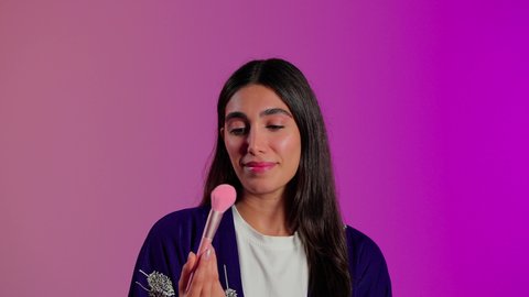 تطبيق المكياج ومستحضرات التجميل, مفهوم التزين والتجمل, الاهتمام بالمظهر الخارجي، بورتريه مقرب لامرأة عربية خليجية  سعودية ترتدي الزي الكاجوال تستعمل فرشاة أحمر الخدود, خلفية ملونه