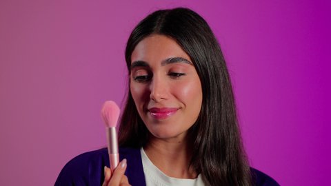 اختيار مستحضرات تجميل تلائم نوع البشرة, مفهوم التزين والتجمل, الاهتمام بالمظهر الخارجي، بورتريه مقرب لامرأة عربية خليجية  سعودية ترتدي الزي الكاجوال تستعمل فرشاة أحمر الخدود, خلفية ملونه