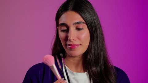 استخدام أدوات التجميل للعناية بالجمال, مفهوم التزين والتجمل, الاهتمام بالمظهر الخارجي، بورتريه مقرب لامرأة عربية خليجية  سعودية ترتدي الزي الكاجوال تستعمل فرشاة أحمر الخدود, خلفية ملونه