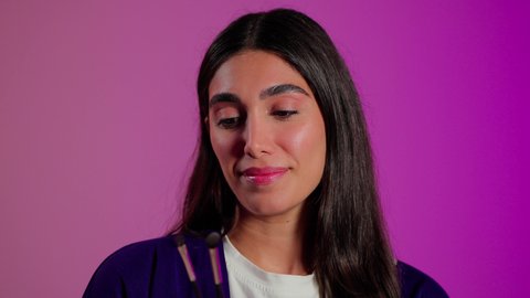 العناية بالجمال والمظهر الخارجي، الترويج لمنتجات و مساحيق التجميل، مفهوم التزين والتجمل، استعمال المستحضرات التجميلية, بورتريه مقرب لامرأة عربية خليجية سعودية ترتدي الزي الكاجوال تستعمل فرشاة ظل العيون, خلفية ملونه