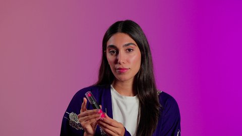 مفهوم التزين والتجمل، استعمال المستحضرات التجميلية, الترويج لمنتجات و مساحيق التجميل, العناية بالجمال والمظهر الخارجي, بورتريه مقرب لامرأة عربية خليجية سعودية ترتدي الزي الكاجوال تضع أحمر شفاه, خلفية ملونه