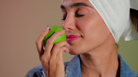 تناول غذاء صحي للحفاظ على الصحة العامة، أهمية وفائدة الفواكه الطازجة للبشرة، فطور وسناك لذيذ، تلبية احيتاجات الجسم من العناصر الغذائية الضرورية, بورتريه مقرب لامرأة عربية خليجية سعودية ترتدي الزي الكاجوال تضع منشفة بيضاء على رأسها تمسك تفاحة خضراء، خلفية ملونه