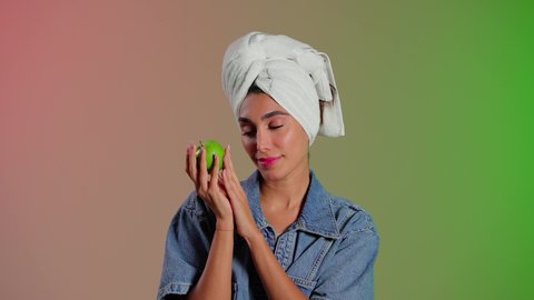 الحفاظ على نظام غذائي متوازن وصحي، أهمية وفائدة الفواكه الطازجة للبشرة، فطور وسناك لذيذ، تلبية احيتاجات الجسم من العناصر الغذائية الضرورية, بورتريه مقرب لامرأة عربية خليجية سعودية ترتدي الزي الكاجوال تضع منشفة بيضاء على رأسها تمسك تفاحة خضراء، خلفية ملونه