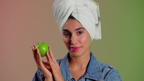 أهمية وفائدة الفواكه الطازجة للبشرة، فطور وسناك لذيذ، تلبية احيتاجات الجسم من العناصر الغذائية الضرورية, بورتريه مقرب لامرأة عربية خليجية سعودية ترتدي الزي الكاجوال تضع منشفة بيضاء على رأسها تمسك تفاحة خضراء، اتباع نظام غذائي صحي، خلفية ملونه
