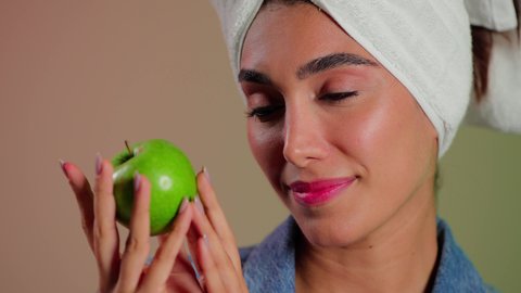 فطور وسناك لذيذ، تلبية احيتاجات الجسم من العناصر الغذائية الضرورية, بورتريه مقرب لامرأة عربية خليجية سعودية ترتدي الزي الكاجوال تضع منشفة بيضاء على رأسها تمسك تفاحة خضراء، اتباع نظام غذائي صحي، أهمية وفائدة الفواكه الطازجة للبشرة، خلفية ملونه