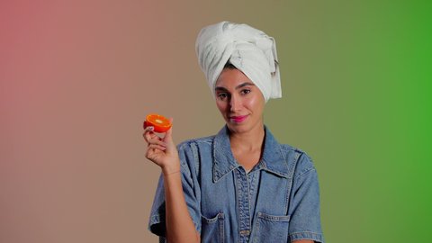 اتباع نظام غذائي صحي، فطور وسناك لذيذ، تلبية حاجة الجسم من العناصر الغذائية, بورتريه لامرأة عربية خليجية سعودية ترتدي الزي الكاجوال تضع منشفة بيضاء على رأسها تمسك بيديها شرائح من البرتقال تضعها أمام عينها، أهمية الفواكه الطازجة للبشرة، خلفية ملونة