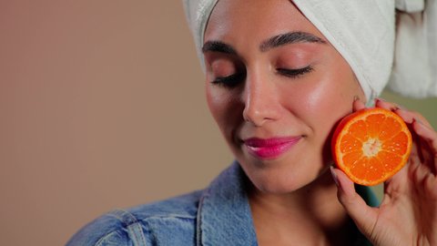 مفهوم العناية بنضارة ونظافة البشرة، بورتريه مقرب لامرأة عربية خليجية سعودية  تضع منشفة بيضاء على رأسها تمسك بيديها شريحه برتقال قطنه تقوم بمسح وجهها، إزالة المكياج باستخدام ضمادات قطنية، الاهتمام بالمظهر الخارجي، خلفية ملونه