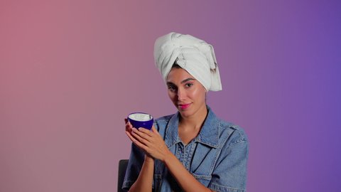 Applying moisturizer after cleansing to maintain softness, the concept of caring for the freshness and improvement of the skin, attention to external appearance, a close-up portrait of a Saudi Gulf Arab woman wearing a white towel applying moisturizer, colorful background.
