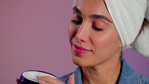 ترطيب الوجه بالكريمات المناسبة لنوع البشرة، مفهوم العناية بنضارة وتحسين البشرة، الاهتمام بالمظهر الخارجي، بورتريه مقرب لامرأة عربية خليجية سعودية ترتدي  منشفة بيضاء تضع كريم مرطب، خلفية ملونه