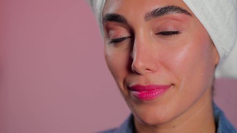 الاهتمام بالمظهر الخارجي، تدليك و ترطيب الوجه، مفهوم العناية بنضارة وتحسين البشرة، بورتريه مقرب لامرأة عربية خليجية سعودية ترتدي  منشفة بيضاء تضع كريم مرطب، استخدام كريمات و مكونات تجميلية، خلفية ملونه