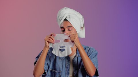 Enhancing skin health and its radiant appearance, steps for cleansing and exfoliating the skin, using a cosmetic ingredient and product, a close-up portrait of a Saudi Gulf Arab woman wearing a head towel applying a mask to her face, colorful background.
