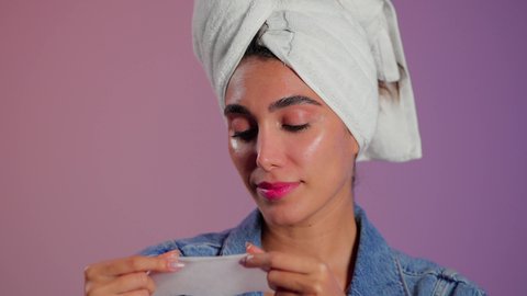 الاهتمام بالبشرة من خلال تنظيف وترطيب فعال، خطوات تنظيف وتقشير البشرة، استخدام مكون ومستحضر تجميلي، بورتريه مقرب لامرأة عربية خليجية سعودية ترتدي منشفة الرأس  تقوم بوضع قناع على وجهها، خلفية ملونه