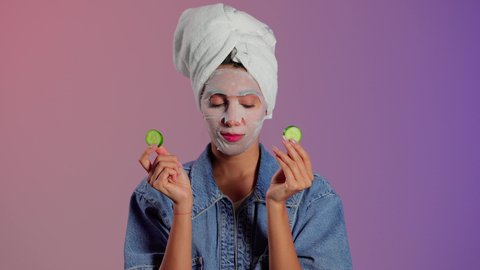 العناية اليومية للبشرة لتحسين ملمسها ولونها، بورتريه مقرب لمرأة عربية خليجية سعودية ترتدي منشفة الرأس تضع القناع التجميلي على الوجه مع قناع الخيار للعيون، إستخدام مكونات تجميلية، خلفية ملونه