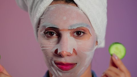 تحسين مظهر البشرة والحفاظ على إشراقتها، بورتريه مقرب لمرأة عربية خليجية سعودية ترتدي منشفة الرأس تضع القناع التجميلي على الوجه مع قناع الخيار للعيون، إستخدام مكونات تجميلية، خلفية ملونه