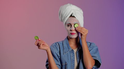 العناية بصحة وجمال البشرة، بورتريه مقرب لمرأة عربية خليجية سعودية ترتدي منشفة الرأس تضع القناع التجميلي على الوجه مع قناع الخيار للعيون، إستخدام مكونات تجميلية، خلفية ملونه