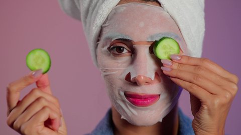 الحفاظ على البشرة ناعمة ومشرقة، بورتريه مقرب لمرأة عربية خليجية سعودية ترتدي منشفة الرأس تضع القناع التجميلي على الوجه مع قناع الخيار للعيون، إستخدام مكونات تجميلية، خلفية ملونه