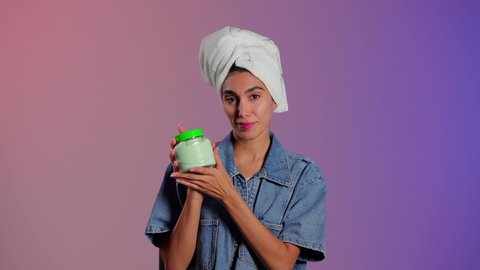 الحفاظ على إشراقة البشرة وصحة خلاياها ،الاهتمام بالأناقة والمظهر الخارجي، بورتريه مقرب لامرأة عربية خليجية سعودية ترتدي منشفة بيضاء على رأسها تضع كريم الترطيب على وجهها، استخدام مستحضر ومكون تجميلي، خلفية ملونه