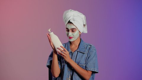 The use of a cosmetic product and ingredient, the concept of caring for and improving skin freshness, a depiction of a Gulf Arab Saudi woman wearing casual attire and a head towel holding a bottle of moisturizing cream and applying it to her hands, with a colorful background.