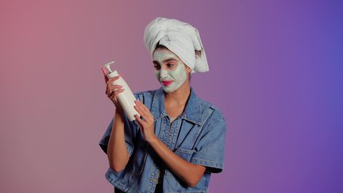 مستحضر تجميلي نسائي، مفهوم العناية والاهتمام بنضارة البشرة وتحسينها، استخدام الكريمات ومكونات التجميل الشبابية، تصوير مقرب امراة عربيه خليجيه سعودية ترتدي الزي الكاجوال و منشفة الرأس تحمل عبوة كريم مرطب و تقوم بوضعه على يديها، خلفية ملونه