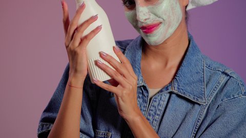 مفهوم العناية والاهتمام بنضارة البشرة وتحسينها، استخدام الكريمات ومكونات التجميل الشبابية، تصوير مقرب لامراة عربيه خليجيه سعودية ترتدي الزي الكاجوال و منشفة الرأس تحمل عبوة كريم مرطب و تقوم بوضعه على يديها، خلفية ملونه