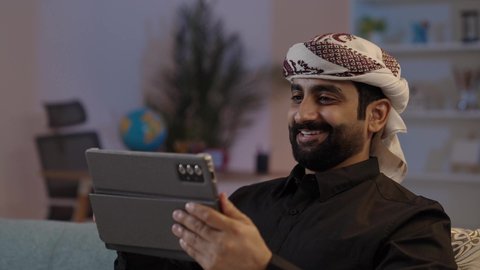 رجل عربي يمني يرتدي القميص والازار مع العمامة يمسك بيده جهاز تابلت بإيماءات الجدية والتركيز، دمج العمل مع التقنية و التكنولوجيا، استعمال التكنولوجيا الحديثة، تصفح تطبيقات التواصل الاجتماعي، استخدام الجهاز اللوحي في إنجاز مهام العمل