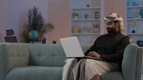 رجل عربي يمني يرتدي القميص والازار مع العمامة  يجلس على اريكة مريحة يقوم بالعمل على الحاسب المحمول، إنجاز مهام الأعمال عن بعد، إدارة شؤون الأعمال وتنظيمها، كتابة وإدخال المعلومات عبر الكيبورد، استخدام التقنيات الحديثة المتطورة، عقد إجتماع عمل عبر الإنترنت