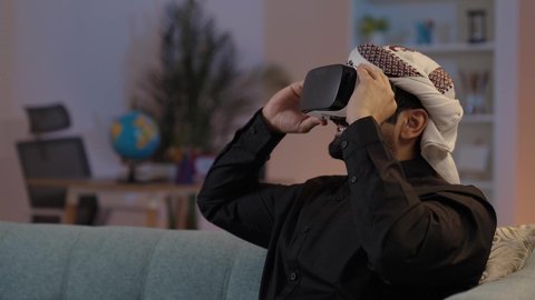 A Yemeni Arab man is watching movies through virtual reality glasses, enjoying and entertaining himself with films, interacting and simulating a fantasy world. A Yemeni man wearing a shirt and a sarong with a turban and 3D virtual reality glasses, simulating the virtual world, using 3D VR technology.