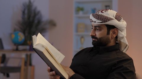 A Yemeni Arab man wearing a shirt and a sarong sits holding a book, spending his free time on learning and culture, focusing on browsing useful books, engaging himself in reading and education, the concept of contemplation and thinking, representing authentic Arab masculinity, preserving traditional attire, the concept of dignity and elegance.