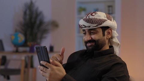 رجل عربي يمني يرتدي القميص والازار مع العمامة يجلس ويحمل الهاتف المحمول،مكالمة فيديوعبر جهاز تقني حديث، تبادل الأحاديث و الأخبار الجيدة، إيماءات السعادة بالتواصل مع الأصدقاء والأقارب، تمثيل الرجولة العربية الأصيلة،  المحافظة على اللباس التقليدي ، مفهوم الهيبة والاناقة