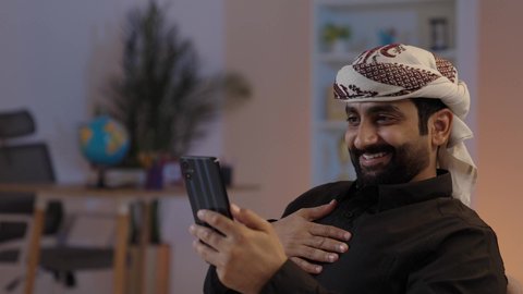 رجل عربي يمني يرتدي القميص والازار مع العمامة يجلس ويحمل الهاتف المحمول، القاء التحية خلال مكالمة فيديو، تبادل الأحاديث و الأخبار الجيدة، إيماءات السعادة بالتواصل مع الأصدقاء والأقارب، تمثيل الرجولة العربية الأصيلة،  المحافظة على اللباس التقليدي ، مفهوم الهيبة والاناقة