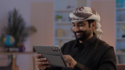 رجل عربي يمني يرتدي القميص والازار مع العمامة يمسك بيده جهاز تابلت بإيماءات الجدية والتركيز دمج التقنية في الحياة اليومية، استعمال التكنولوجيا الحديثة، تصفح تطبيقات التواصل الاجتماعي، استخدام الجهاز اللوحي في إنجاز مهام العمل