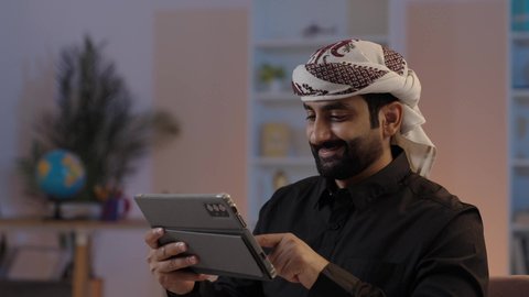 رجل عربي يمني يرتدي القميص والازار مع العمامة يمسك بيده جهاز تابلت بإيماءات الجدية والتركيز النقر على جهاز التابلت،، استعمال التكنولوجيا الحديثة، تصفح تطبيقات التواصل الاجتماعي، استخدام الجهاز اللوحي في إنجاز مهام العمل