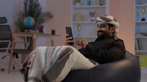 رجل عربي يمني يرتدي القميص والازار مع العمامة يجلس ويحمل الهاتف المحمول،  تبادل الأخبار والأحاديث، تبادل الأحاديث و الأخبار الجيدة، إيماءات السعادة بالتواصل مع الأصدقاء والأقارب، تمثيل الرجولة العربية الأصيلة، المحافظة على اللباس التقليدي