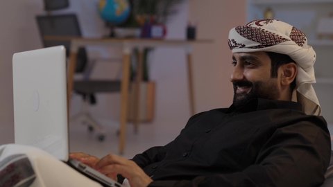 رجل عربي يمني يرتدي القميص والازار مع العمامة  يجلس على كرسي مريح يقوم بالعمل على الحاسب المحمول ايماءات السرور والسعادة، إدارة شؤون الأعمال وتنظيمها، كتابة وإدخال المعلومات عبر الكيبورد، استخدام التقنيات الحديثة المتطورة، عقد إجتماع عمل عبر الإنترنت