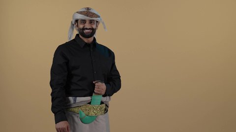 رجل عربي يمني مبتسم يرتدي القميص والازار مع العمامة والجنبية يرفع أصبعه الابهام بعلامة الجودة,الاعجاب والقبول والموافقة, السرور والفرح بتحقيق الاهداف و نيل المراد،  حركة يد وايماءات وجه تدل على الإعجاب والموافقة، خلفية بيج