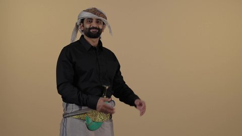 رجل  عربي يمني مبتسم يرتدي القميص الازار مع العمامة والجنبية يقوم بتحريك يديه والاشارة ترحيب بالضيوف، تعابير الترحيب والاستقبال، إلقاء التحية والسلام، مفهوم العلاقات الاجتماعية، المحافظة على اللباس التقليدي، مفهوم الهيبة والرجولة، خلفية بيج