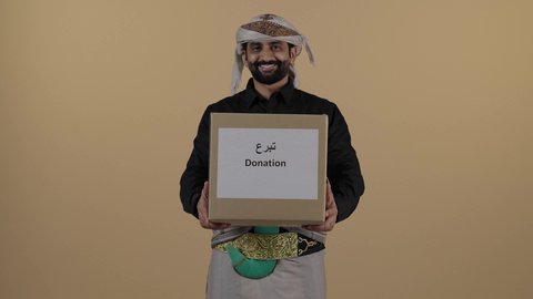 بورتريه لرجل عربي يمني يرتدي االقميص والازار مع العمامة والجنبية يحمل صندوق من الثياب، تبرعات ومبادرات انسانية, توفير المستلزمات الضرورية للفقراء، جمعية خيرية ومبادرة انسانية في اليمن، تأمين الملابس وإهدائها للمحتاجين، مفهوم المساعدة والتبرع، خلفية بيج
