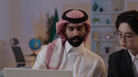 عقد اتفاقيات عمل جديدة، استضافة رجال الاعمال الاجانب في المملكة, استخدام التقنية الحديثة في انجاز العمل، تبادل الخبرات والمعرفة بين البلاد, رجل عربي خليجي سعودي يرتدي الزي التقليدي مع شاب صيني يرتدي البدلة الرسمية يقومان برؤية مشروع ما على اللابتوب المحمول