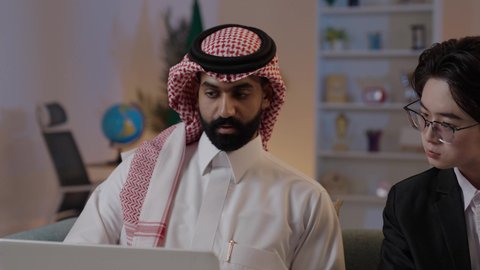 عقد اتفاقيات عمل جديدة، استضافة رجال الاعمال الاجانب في المملكة, استخدام التقنية الحديثة في انجاز العمل، تبادل الخبرات والمعرفة بين البلاد, رجل عربي خليجي سعودي يرتدي الزي التقليدي مع شاب صيني يرتدي البدلة الرسمية يقومان برؤية مشروع ما على اللابتوب المحمول