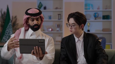 استخدام التقنية الحديثة في انجاز العمل، تبادل الخبرات والمعرفة بين البلاد, عقد اتفاقيات عمل جديدة، استضافة رجال الاعمال الاجانب في المملكة, رجل عربي خليجي سعودي يرتدي الزي التقليدي مع شاب صيني يرتدي البدلة الرسمية يقومان برؤية مشروع ما على التابليت المحمول