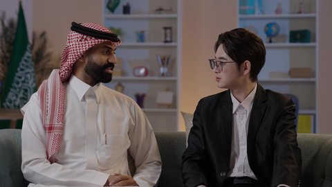 ايماءات السعادة والسرور، استضافة رجال الاعمال الاجانب في المملكة العربية السعودية، تبادل الخبرات والمعرفة بين البلاد، رجل عربي خليجي سعودي يرتدي الزي التقليدي مع شاب صيني يرتدي البدلة الرسمية يقومان بالتحدث وتبادل لاخبار