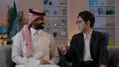 ايماءات السعادة والسرور، استضافة رجال الاعمال الاجانب في المملكة العربية السعودية، تبادل الخبرات والمعرفة بين البلاد، رجل عربي خليجي سعودي يرتدي الزي التقليدي مع شاب صيني يرتدي البدلة الرسمية يقومان بالتحدث وتبادل لاخبار