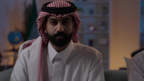 ايماءات السعادة بالفوز والانتصار، استضافة رجال الاعمال الاجانب في المملكة العربية السعودية، رجل عربي خليجي سعودي يرتدي الزي التقليدي يجلس مع شاب صيني يرتدي البدلة الرسمية ، فوز الفريق المفضل، مشاهدة مباراة الفريق اللمفضل