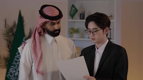 اعداد تقارير العمل، تبادل الخبرات والمعرفة بين البلاد، استضافة رجال الاعمال الاجانب في المملكة العربية السعودية، رجل عربي خليجي سعودي يرتدي الزي التقليدي مع شاب صيني يرتدي البدلة الرسمية يقومان بمناقشة المشاريع، المناقشة في اهداف الشركة