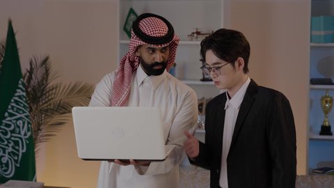 عقد اتفاقيات عمل جديدة، استضافة رجال الاعمال الاجانب في المملكة العربية السعودية, تبادل الخبرات والمعرفة بين البلاد, رجل عربي خليجي سعودي يرتدي الزي التقليدي مع شاب صيني يرتدي البدلة الرسمية يقومان بالعمل على اللابتوب المحمول